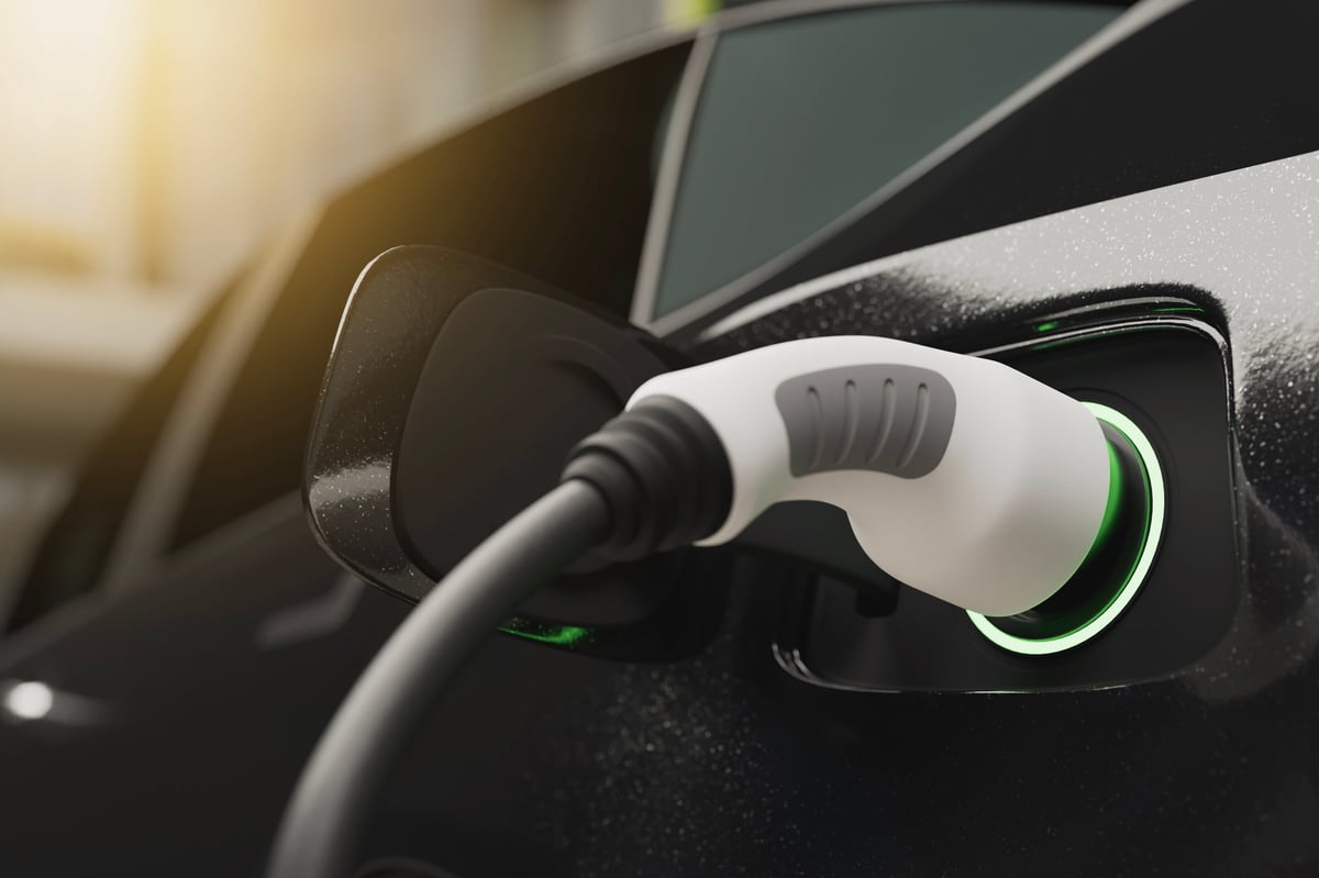 Nahaufnahme eines Ladesteckers in der Ladebuchse eines dunklen Elektroautos, der Ring um die Buchse leuchtet grün